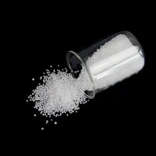 White technical grade urea crystals spilling from a glass beaker